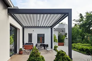 Bioklimatische Pergola mit drehbaren Sonnenschutzlamellen auf einer modernen Terrasse neben einem Garten mit üppiger Vegetation.